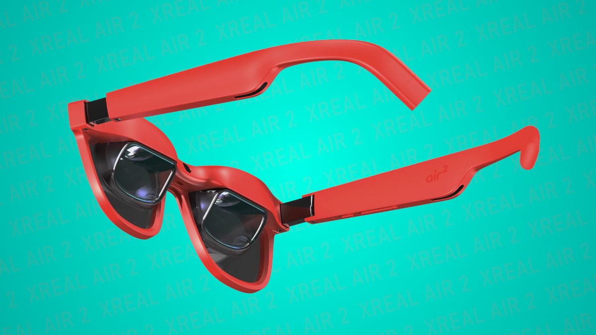 Image of XREAL Air 2 AR glasses, wearable displays that use bird bath optics to superimpose content into your field of vision, in red showing a 3/4 rear view of the optics and frames on a teal backdrop with the words 'XREAL Air 2' repeated in the background.